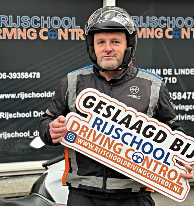 Geslaagde motorleerling Dennis met helm en Geslaagd-bord voor kantoor Rijschool Driving Control Rotterdam