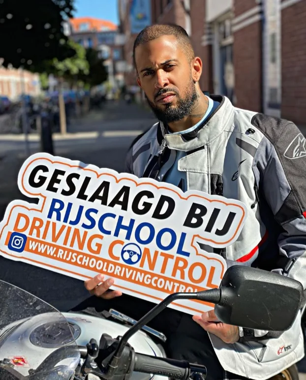 Geslaagde motorleerling Kevin in motorkleding met Geslaagd-bord Rijschool Driving Control Rotterdam