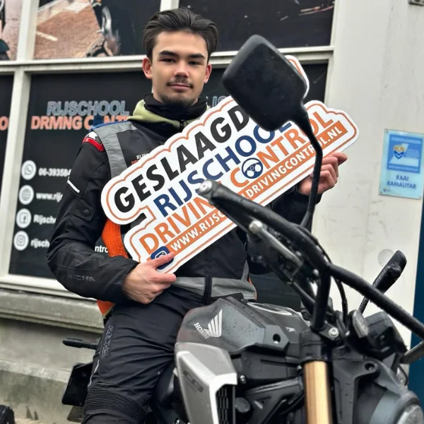 Geslaagde motorleerling Rayan met Geslaagd-bord bij Rijschool Driving Control Rotterdam