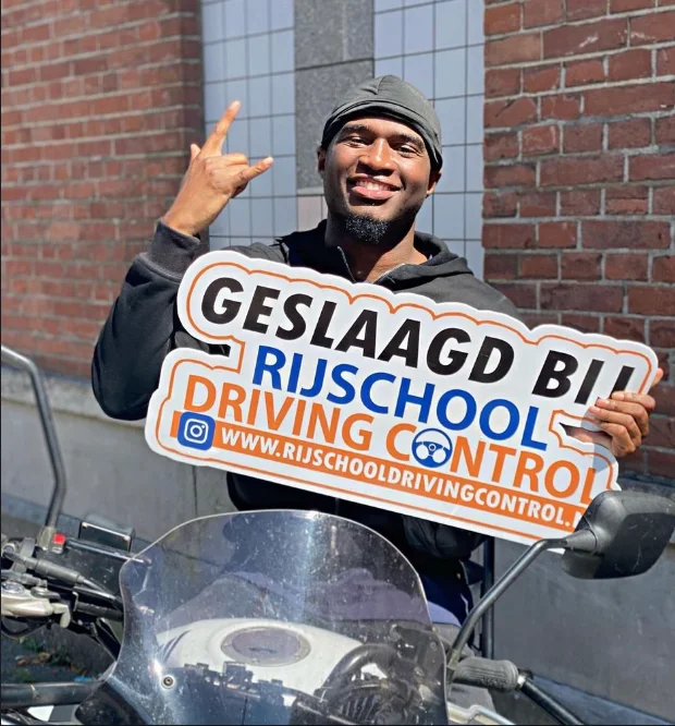 Geslaagde motorleerling Jamal met Geslaagd-bord na motorexamen Rotterdam bij Rijschool Driving Control